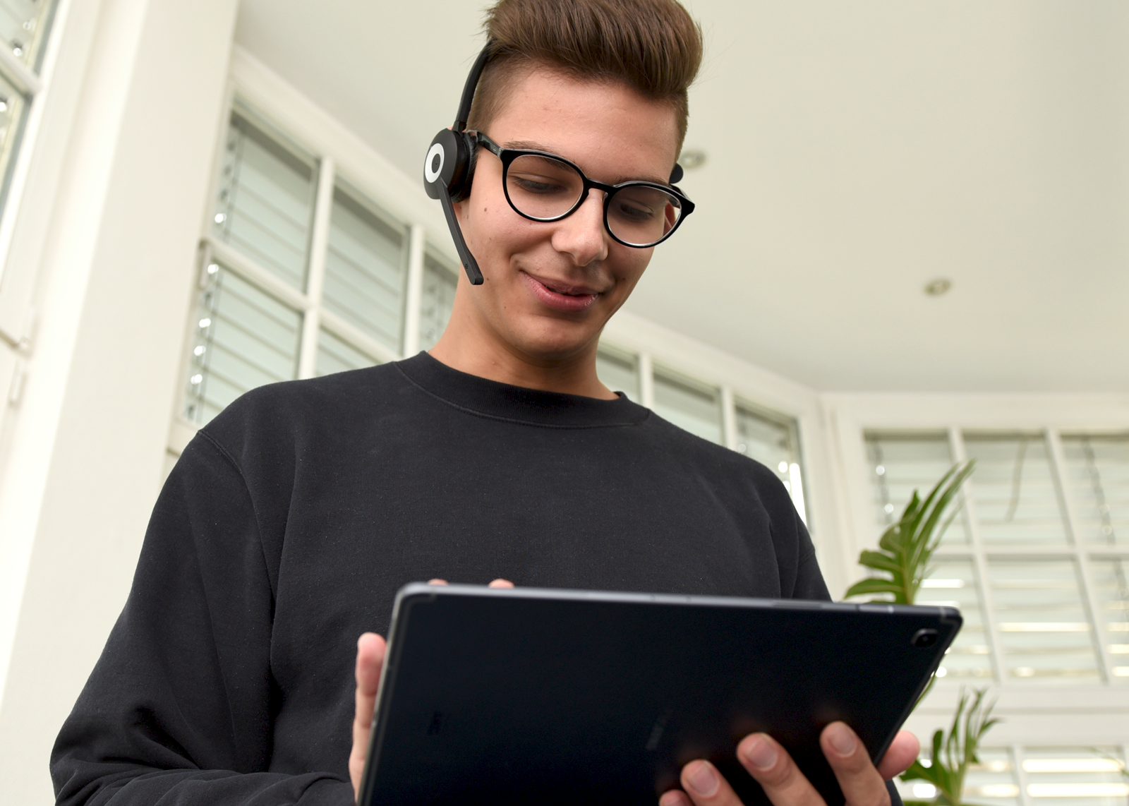 Foto von einem jungen Mann der ein Headset trägt und auf ein Tablet schaut